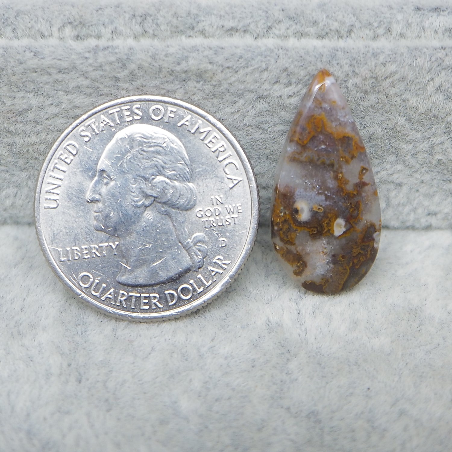 Teardrop-shaped stone next to a U.S. quarter dollar on a textured surface