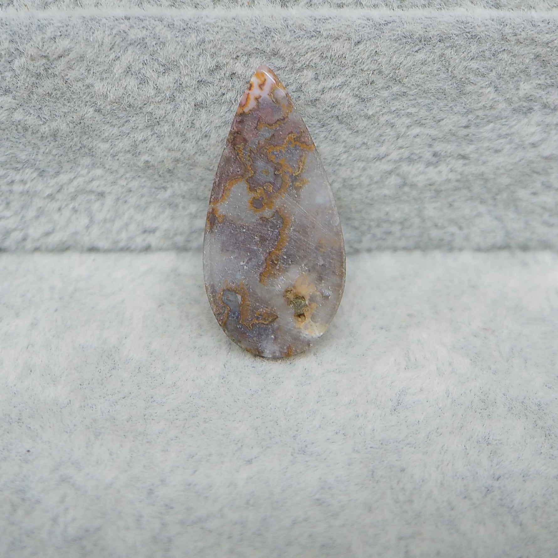 Teardrop-shaped agate stone on a textured gray background