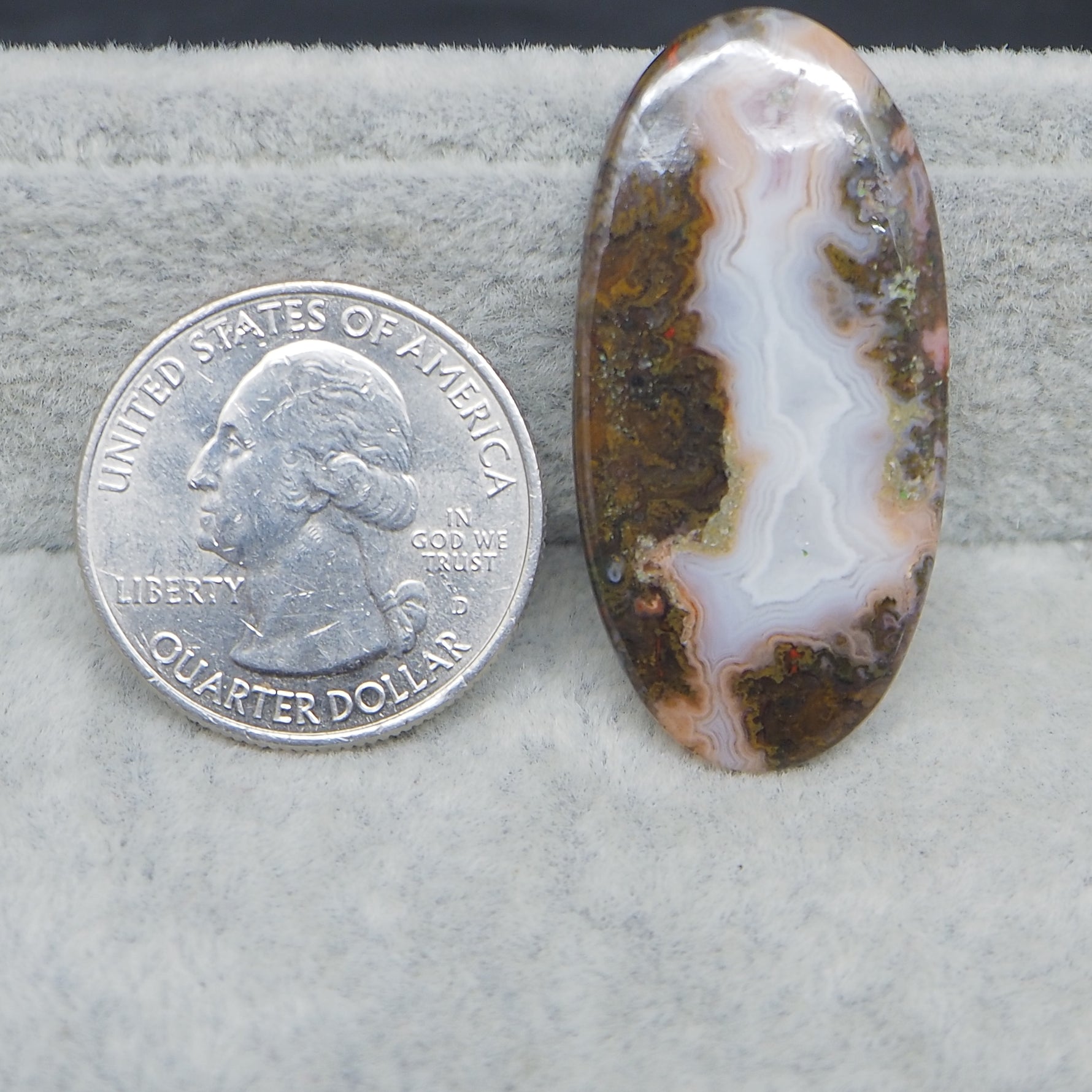 Oval-shaped agate stone next to a U.S. quarter dollar on a gray background