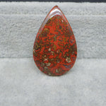 Teardrop-shaped red and brown patterned stone on a gray surface