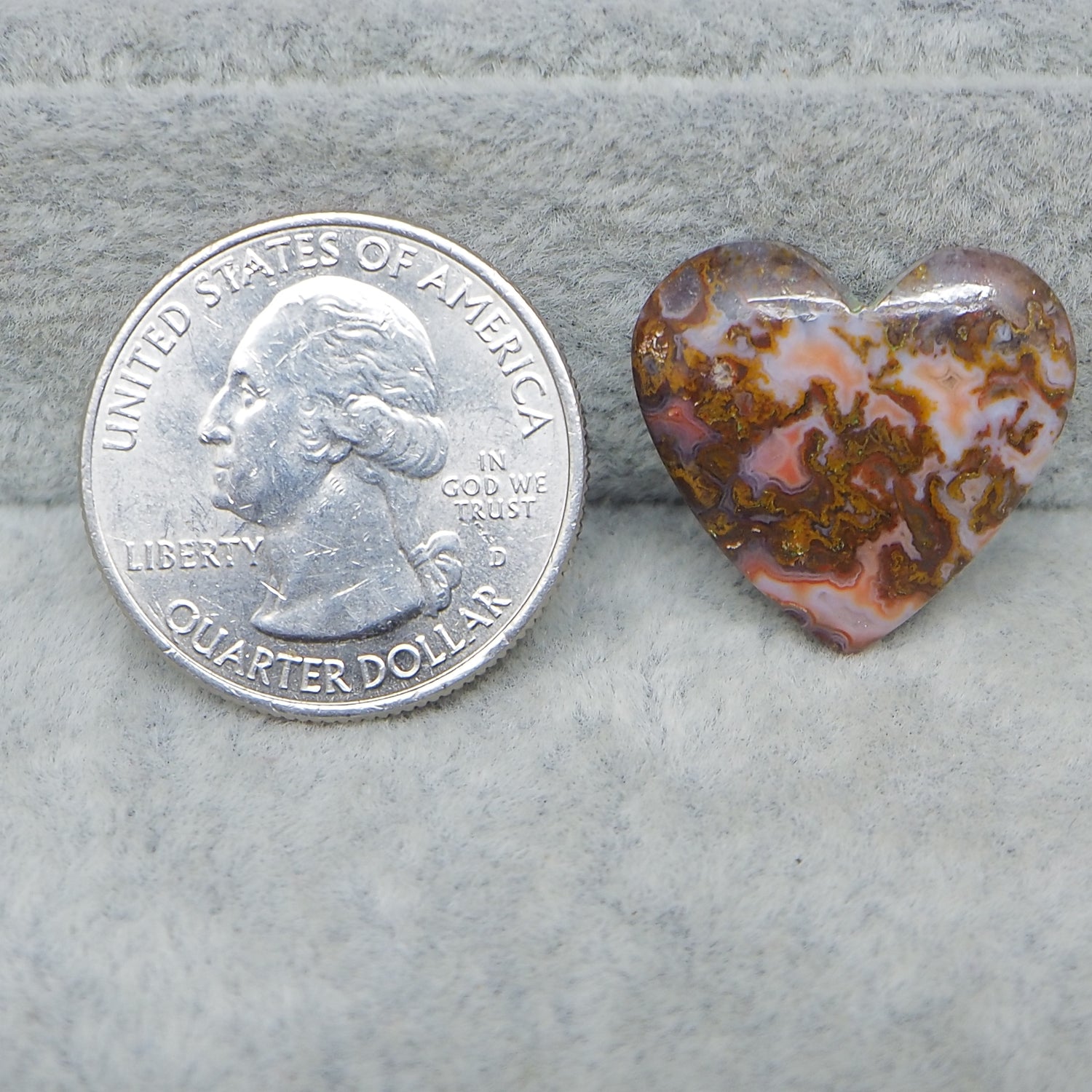 Heart-shaped opal stone next to a U.S. quarter dollar coin on a gray surface