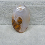 Oval-shaped agate stone with brown patterns on a textured gray background