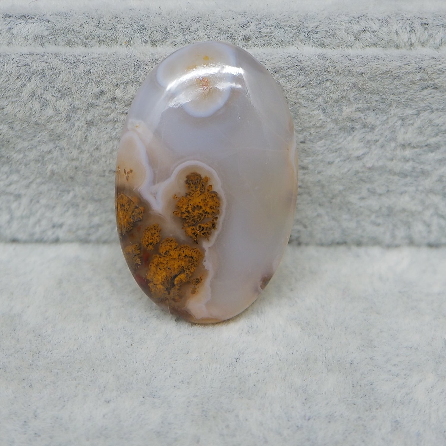 Oval-shaped agate stone with brown patterns on a textured gray background