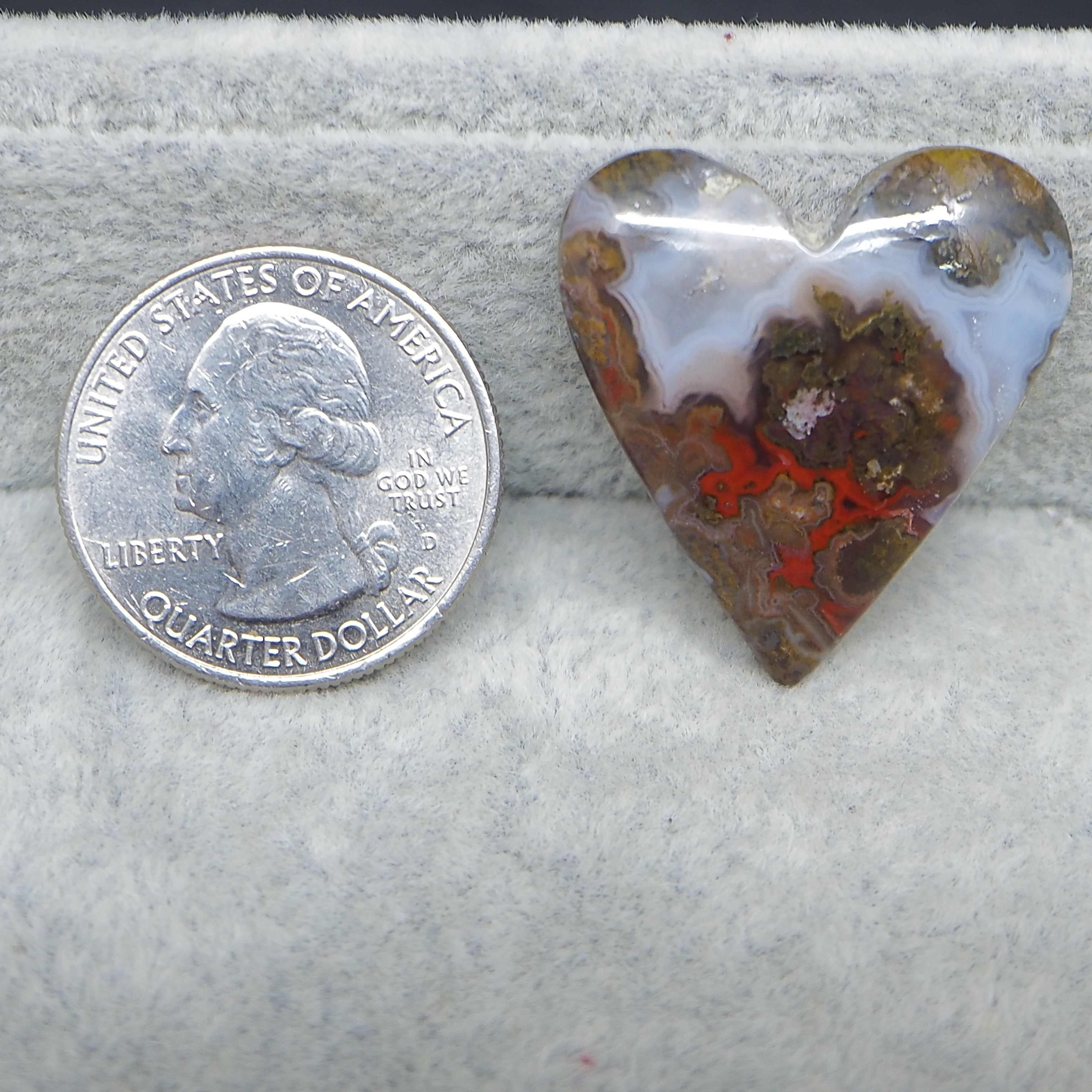 Heart-shaped agate stone next to a U.S. quarter dollar on a gray background