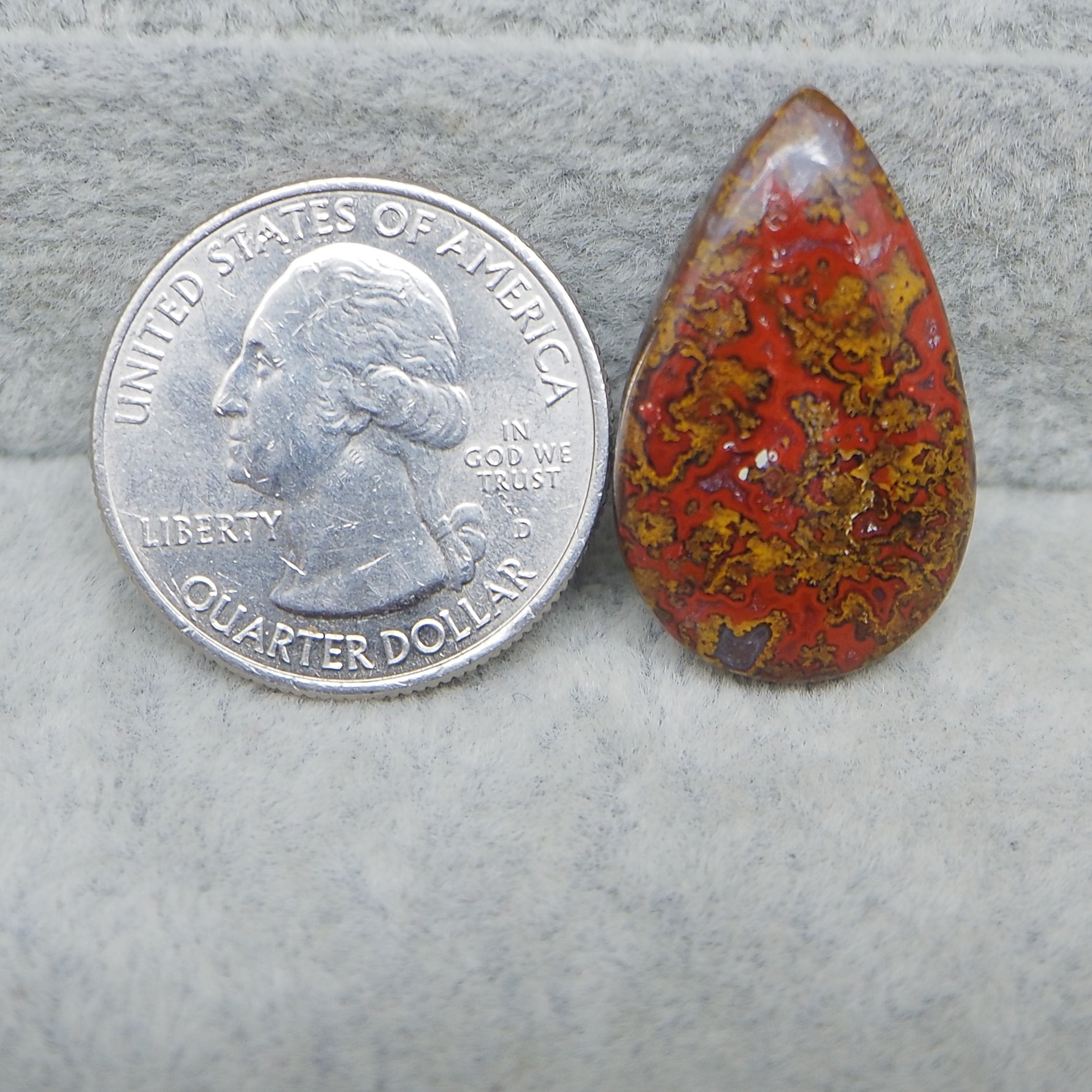 Teardrop-shaped red and brown stone next to a U.S. quarter dollar coin on a gray background