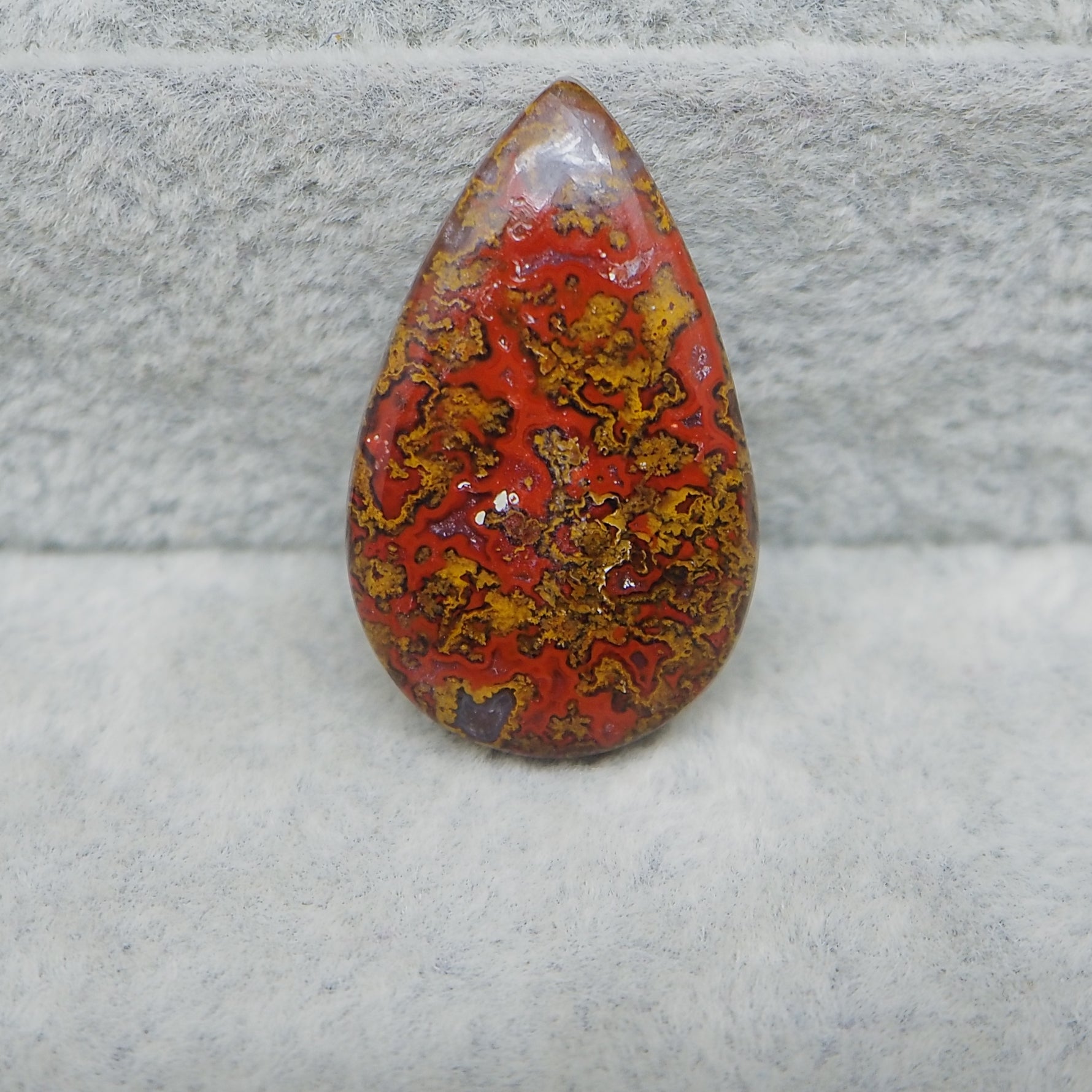 Teardrop-shaped red and yellow patterned stone on a textured gray surface