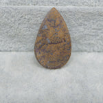 Teardrop-shaped stone with brown and purple hues on a textured gray background