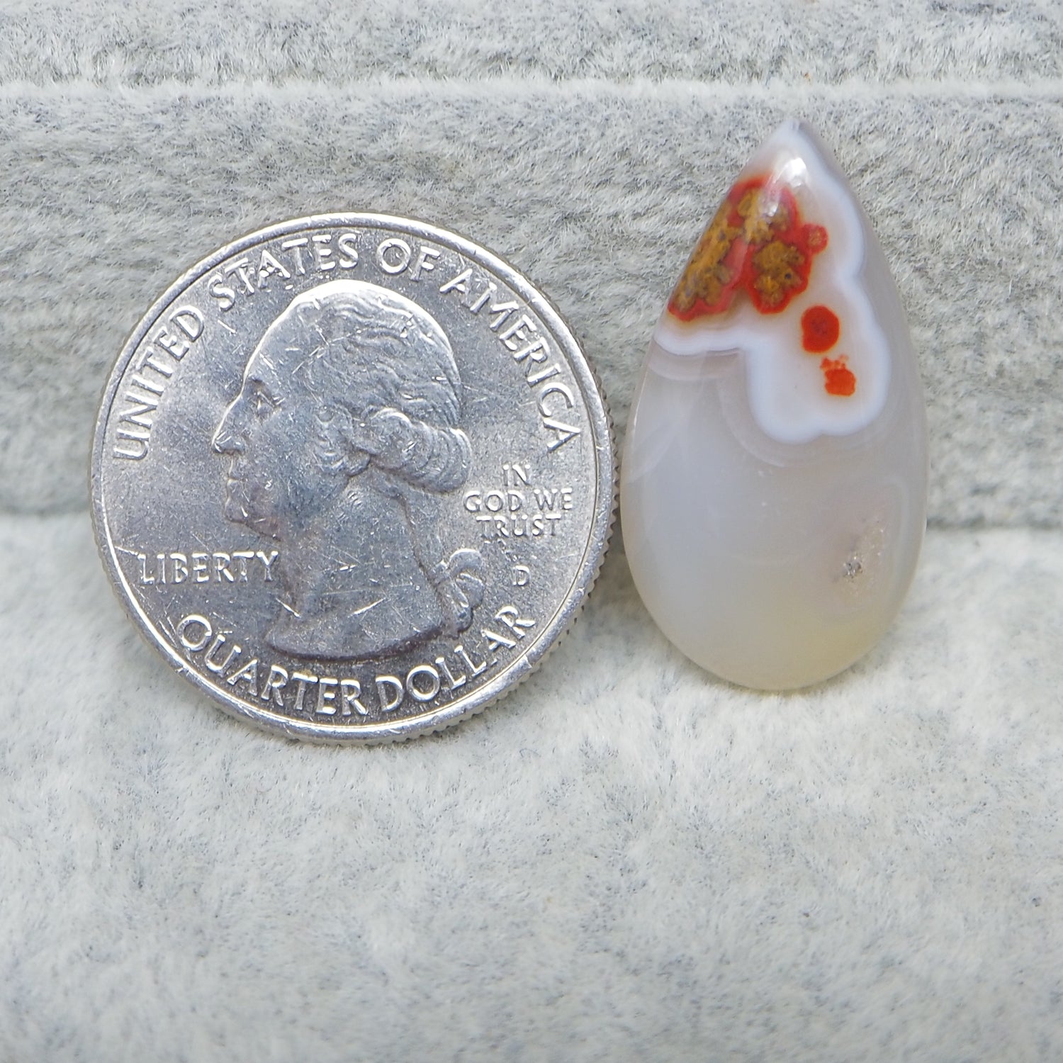 Glass teardrop pendant next to a U.S. quarter dollar coin on a textured surface