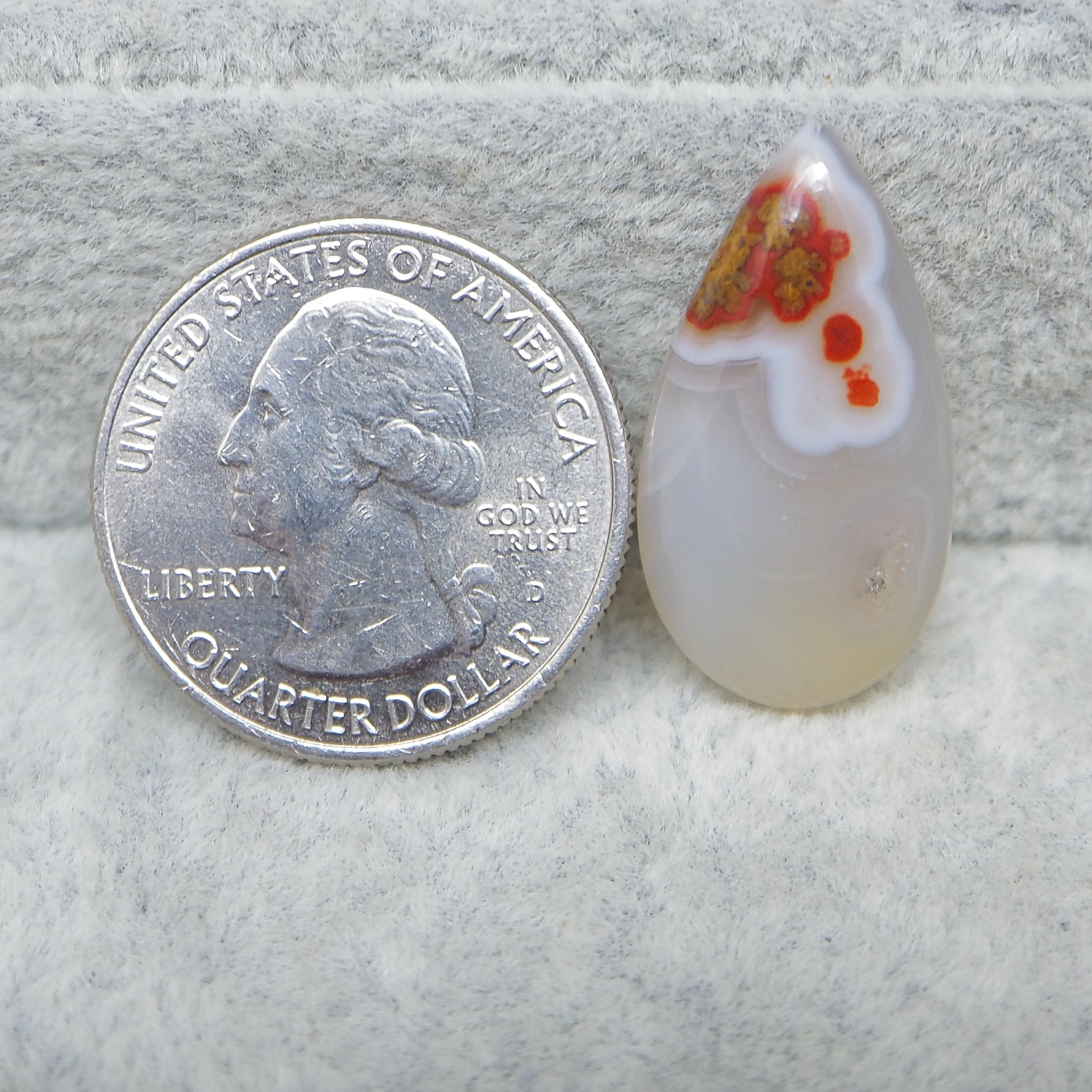 Glass teardrop pendant next to a U.S. quarter dollar coin on a textured surface