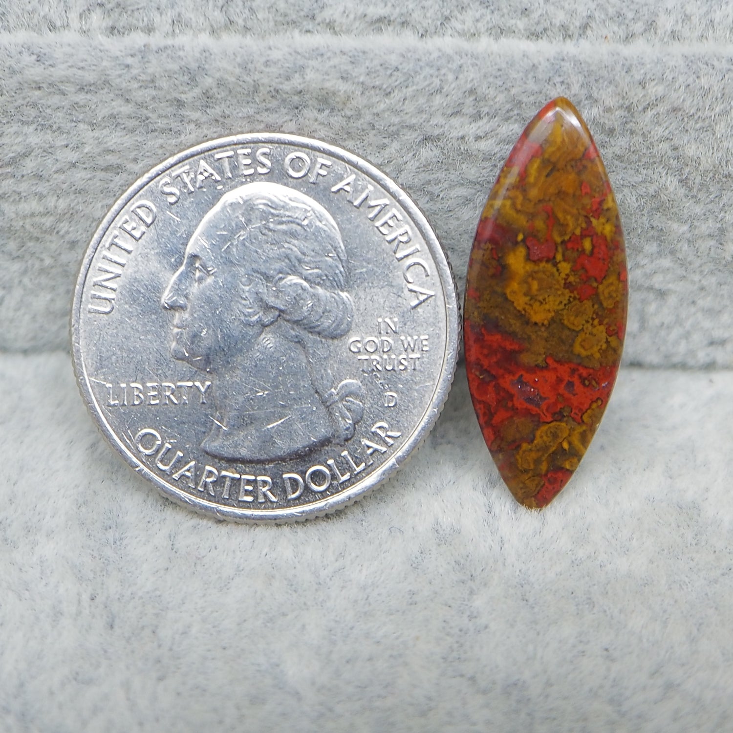 Quarter dollar coin next to a red and brown stone on a gray surface