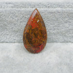 Teardrop-shaped red and brown stone on a gray textured background