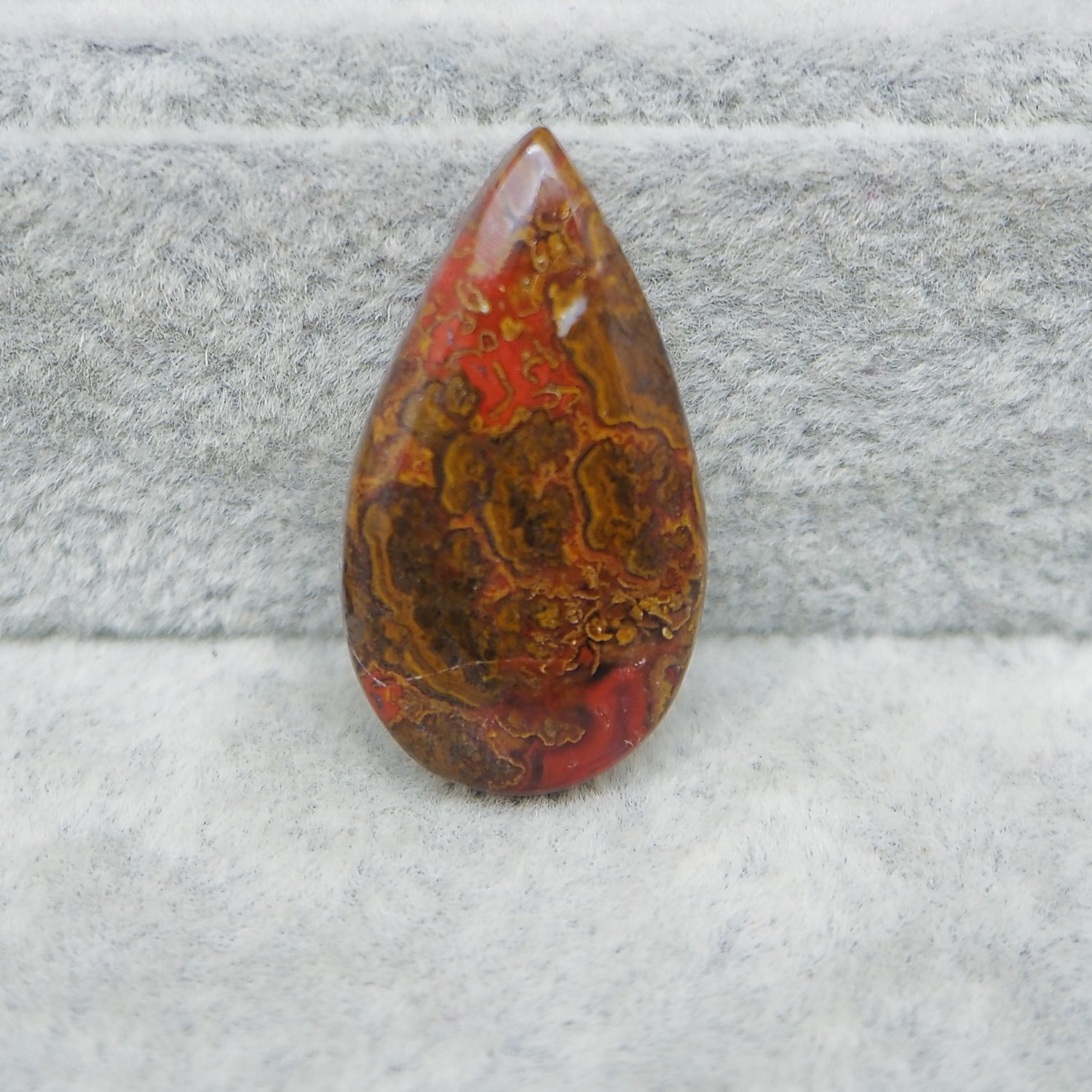 Teardrop-shaped red and brown stone on a gray textured background