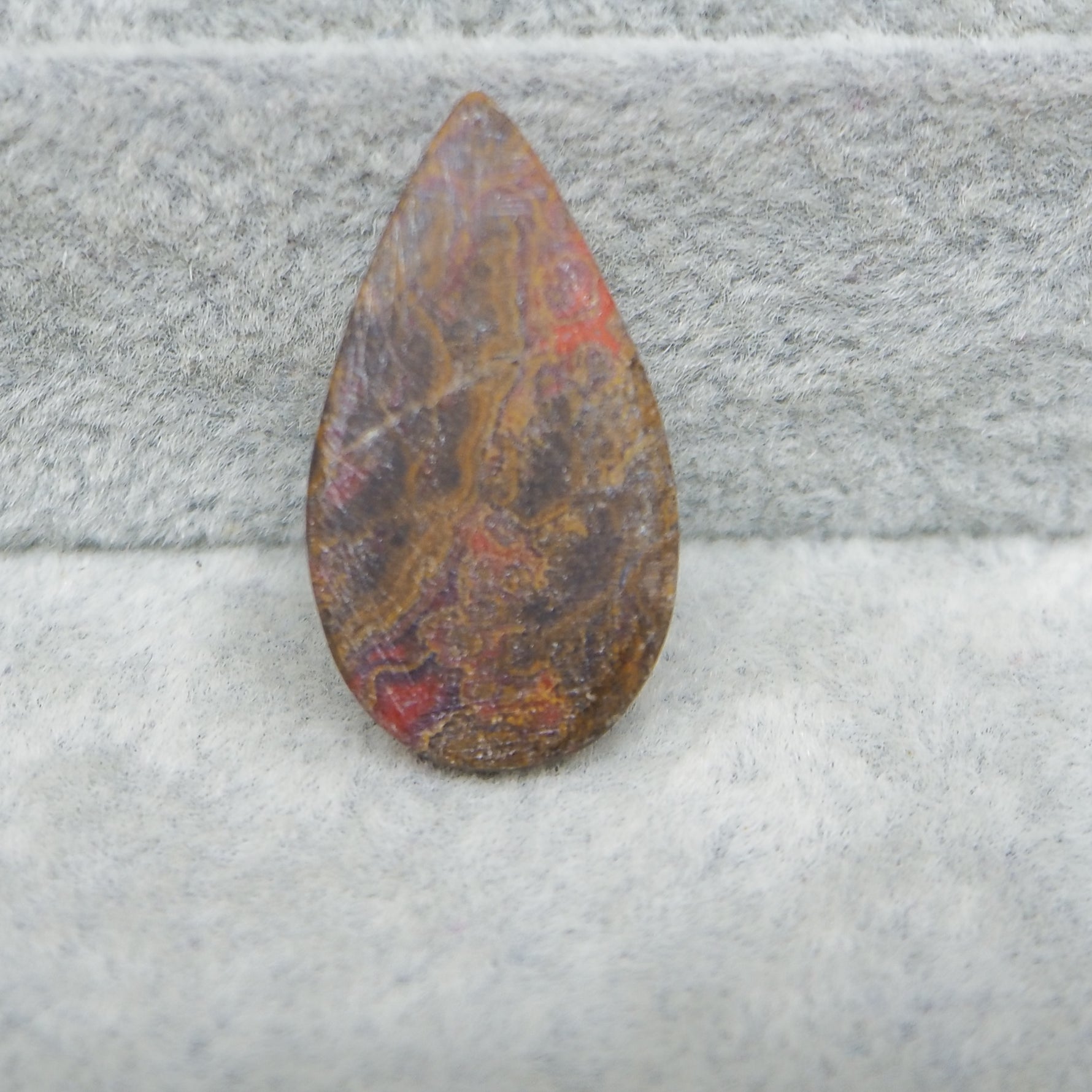 Teardrop-shaped stone with marbled pattern on a textured gray surface