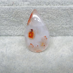 Teardrop-shaped stone with orange and red speckles on a textured gray background
