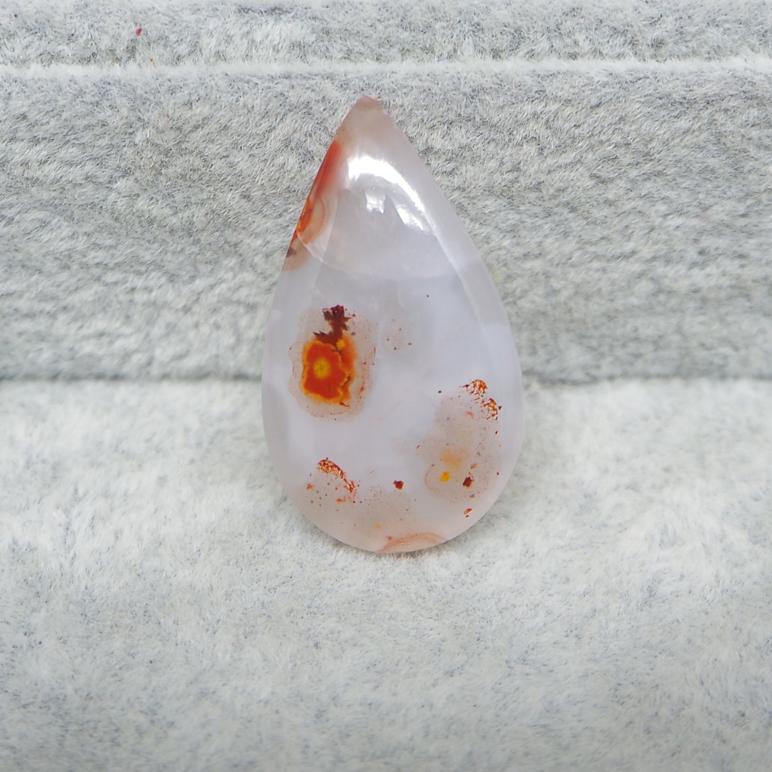 Teardrop-shaped stone with orange and red speckles on a textured gray background