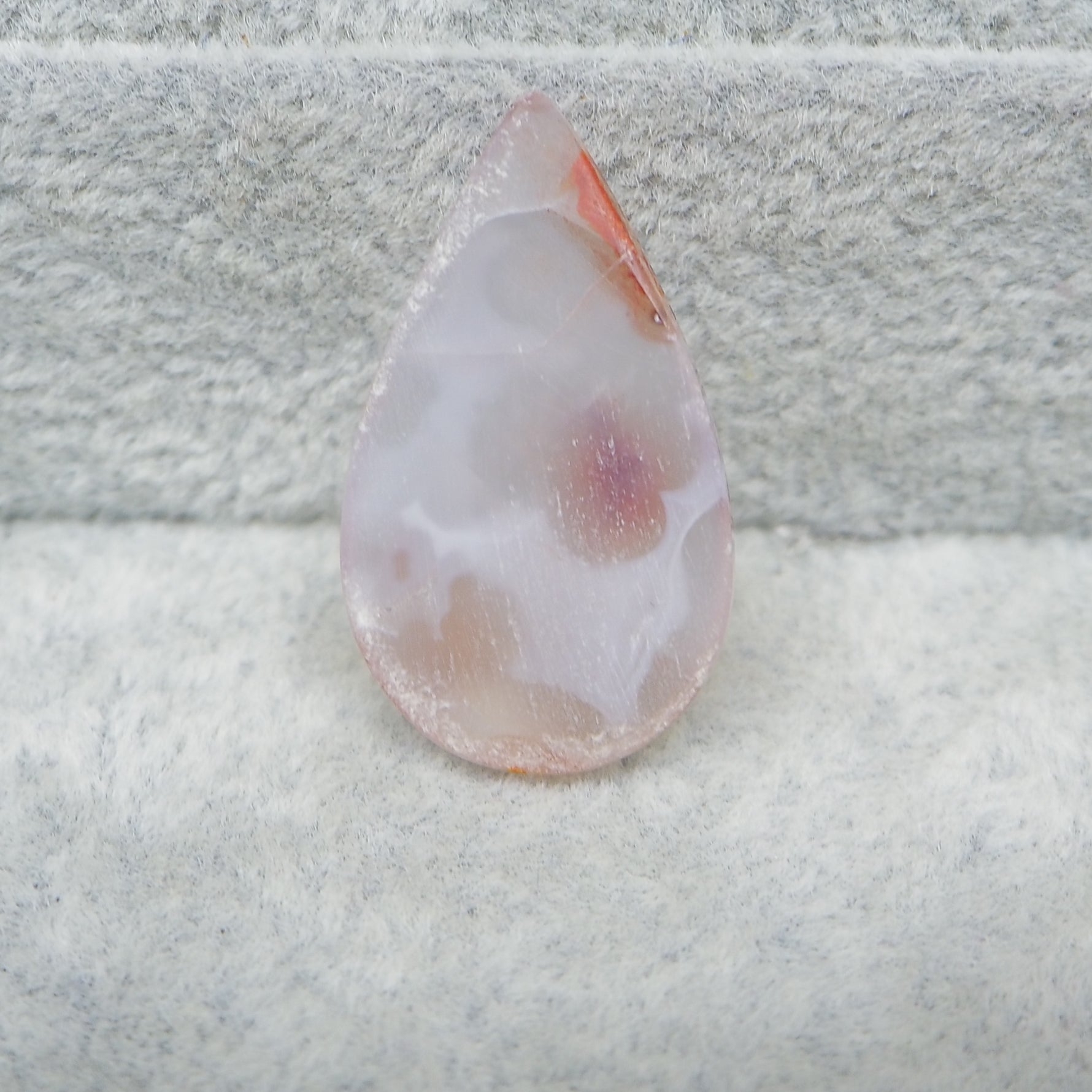 Teardrop-shaped agate stone on a textured gray surface