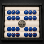 Set of blue dice with red pips in a display case, accompanied by a silver coin.