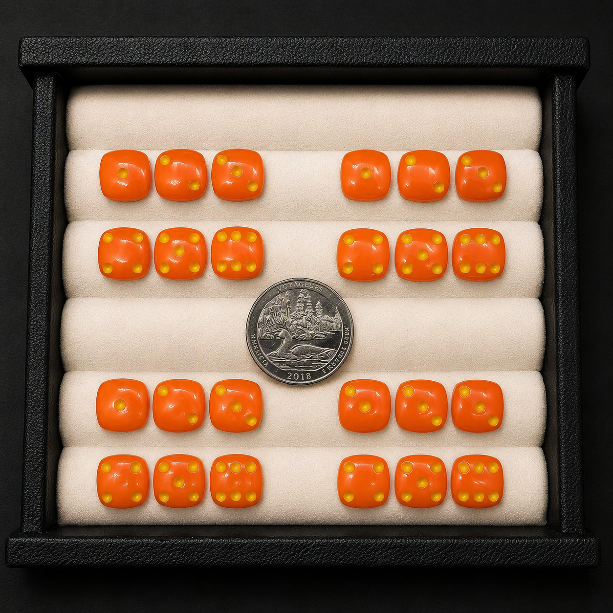 Set of orange dice with yellow pips in a display case with a quarter coin for scale.