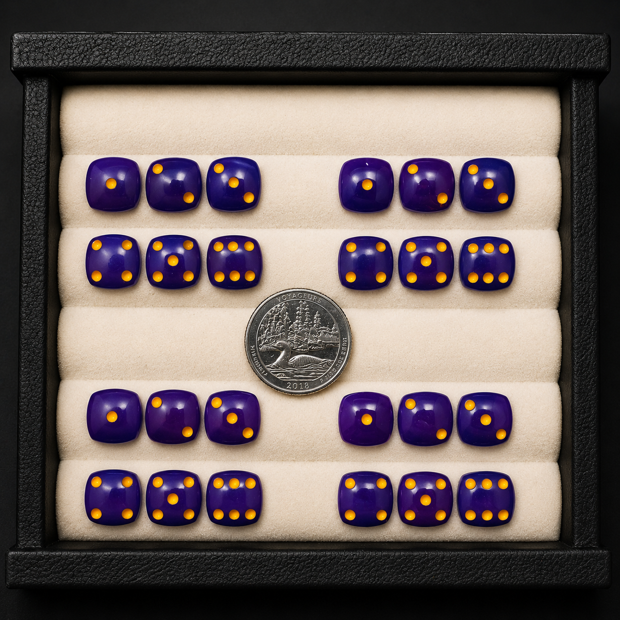 Set of purple dice with yellow dots on a display tray with a coin for scale.