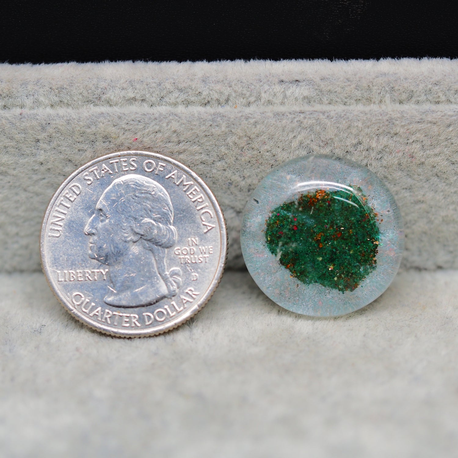 United States quarter dollar coin next to a small round stone with green and red speckles on a textured surface.