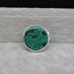 Round green glittery object on a textured gray surface with black background